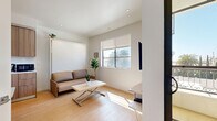 Located on Mayfield Avenue in the desirable Brentwood neighborhood of Los Angeles, this thoughtfully designed studio maximizes every inch of its compact footprint. The open-plan living area is anchored by light hardwood flooring, recessed lighting, and crisp white walls that create a bright, airy atmosphere. Natural light streams in through large windows, offering views of the surrounding palm tree-lined streetscape.

The space is cleverly outfitted with a wall-mounted Murphy bed that doubles as a sofa seating area, allowing seamless transition between living and sleeping functions. A wall-mounted TV and built-in desk shelf provide practical media and workspace solutions. A compact dining area with a fold-out table and chairs sits adjacent to the kitchen cabinetry, which features warm wood-toned finishes and integrated appliances.

A dedicated closet offers organized storage, while the bathroom impresses with its upscale finishes, including large-format beige tiles, a glass-enclosed walk-in shower with a built-in niche, a wall-mounted toilet, and a floating vanity with an undermount sink. A sliding glass door leads to an outdoor access point, adding to the sense of openness. This studio is a well-executed example of modern, efficient design in a prime Los Angeles location.
