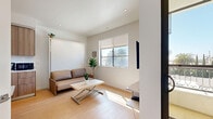 Located on Mayfield Avenue in the desirable Brentwood neighborhood of Los Angeles, this thoughtfully designed studio maximizes every inch of its compact footprint. The open-plan living area is anchored by light hardwood flooring, recessed lighting, and crisp white walls that create a bright, airy atmosphere. Natural light streams in through large windows, offering views of the surrounding palm tree-lined streetscape.

The space is cleverly outfitted with a wall-mounted Murphy bed that doubles as a sofa seating area, allowing seamless transition between living and sleeping functions. A wall-mounted TV and built-in desk shelf provide practical media and workspace solutions. A compact dining area with a fold-out table and chairs sits adjacent to the kitchen cabinetry, which features warm wood-toned finishes and integrated appliances.

A dedicated closet offers organized storage, while the bathroom impresses with its upscale finishes, including large-format beige tiles, a glass-enclosed walk-in shower with a built-in niche, a wall-mounted toilet, and a floating vanity with an undermount sink. A sliding glass door leads to an outdoor access point, adding to the sense of openness. This studio is a well-executed example of modern, efficient design in a prime Los Angeles location.