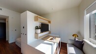 Located at 2215 NW Quimby St in Portland, Oregon, this thoughtfully designed single-floor unit offers a compact yet functional layout with modern finishes throughout. The living area features warm hardwood-style flooring, a built-in wall unit with natural wood floating shelves, and a large window that frames views of the surrounding Portland cityscape, allowing abundant natural light to fill the space.

The kitchen is a standout feature, showcasing rich walnut upper cabinetry paired with deep navy lower cabinets and a bold cobalt blue tile backsplash. Light stone countertops and a gold-toned faucet add refined contrast, while stainless steel appliances — including a gas range, built-in microwave, and dishwasher — provide a full suite of modern conveniences.

A hallway connects the living and kitchen areas to the bathroom and additional spaces, with a closet housing a stacked full-size washer and dryer for in-unit laundry convenience. The bathroom is clean and bright, featuring full white tile surround on the tub/shower combination, warm wood-look flooring, and gold hardware accents that echo the design language found throughout the unit.

Overall, the space presents a cohesive modern aesthetic, balancing functional storage solutions with stylish finishes, making it a well-appointed residence in the heart of Northwest Portland.
