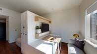 Located at 2215 NW Quimby St in Portland, Oregon, this thoughtfully designed single-floor unit offers a compact yet functional layout with modern finishes throughout. The living area features warm hardwood-style flooring, a built-in wall unit with natural wood floating shelves, and a large window that frames views of the surrounding Portland cityscape, allowing abundant natural light to fill the space.

The kitchen is a standout feature, showcasing rich walnut upper cabinetry paired with deep navy lower cabinets and a bold cobalt blue tile backsplash. Light stone countertops and a gold-toned faucet add refined contrast, while stainless steel appliances — including a gas range, built-in microwave, and dishwasher — provide a full suite of modern conveniences.

A hallway connects the living and kitchen areas to the bathroom and additional spaces, with a closet housing a stacked full-size washer and dryer for in-unit laundry convenience. The bathroom is clean and bright, featuring full white tile surround on the tub/shower combination, warm wood-look flooring, and gold hardware accents that echo the design language found throughout the unit.

Overall, the space presents a cohesive modern aesthetic, balancing functional storage solutions with stylish finishes, making it a well-appointed residence in the heart of Northwest Portland.