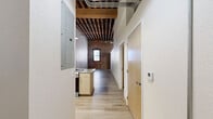 Located at 1601 Walnut St in Kansas City's vibrant Crossroads Arts District, this loft-style unit blends historic industrial character with modern finishes. The open living area makes a striking impression with soaring ceilings that expose original heavy timber rafters and structural beams, alongside visible ductwork that reinforces the space's authentic industrial aesthetic. Original brick masonry and aged wood columns add warmth and texture throughout.

Light-toned luxury vinyl plank flooring runs throughout the main living areas, complementing the bright white walls and creating a clean, contemporary contrast to the raw architectural elements above. The kitchen features light maple cabinetry, neutral countertops, and a full suite of stainless steel appliances including a refrigerator, dishwasher, and range. A peninsula provides additional prep space and a natural division within the open floor plan.

The unit includes two bathrooms, one of which showcases an original brick accent wall and a window, adding character to the functional space. Light wood cabinetry and a well-appointed vanity complete the bath. A walk-in closet with wire shelving and carpeted flooring offers generous storage. The overall layout is efficient yet open, making excellent use of every square foot while preserving the building's historic soul.