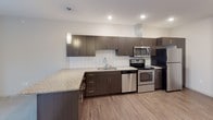 Unit 309 is a thoughtfully designed single-floor residence that combines modern aesthetics with practical functionality. The kitchen serves as a central highlight, showcasing dark espresso cabinetry with sleek brushed-nickel hardware, granite countertops, and a classic white subway tile backsplash. A full suite of stainless steel appliances—including an electric range, over-the-range microwave, dishwasher, and refrigerator—provides a well-equipped cooking space. A pendant light fixture and recessed lighting illuminate the open kitchen layout, which features an extended counter ideal for casual dining or additional prep space.

The flooring transitions from durable wood-look planks in the kitchen and living areas to plush carpeting in the bedroom zones, creating distinct yet cohesive spaces. The bathroom is clean and functional, featuring a soaking tub with shower combination, a dark-cabinetry vanity with granite countertop, and a large mirror with contemporary lighting. A dedicated laundry area houses a stacked full-size washer and dryer alongside wire shelving for added storage. Throughout the residence, neutral white walls and recessed lighting contribute to a bright, modern ambiance.