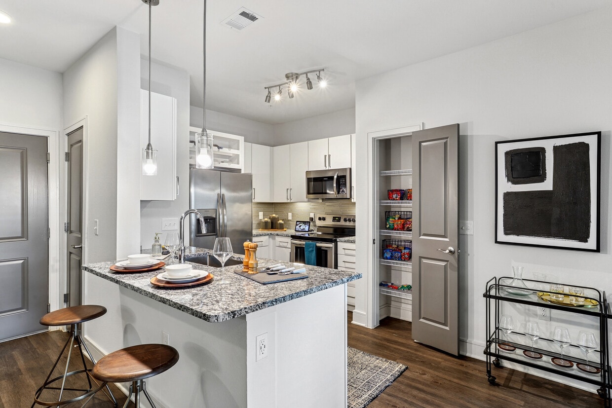 Kitchen with white cabinetry, speckled granite countertops, grey tile backsplash, stainless steel appliances, and hard surface flooring - Avalon Frisco North