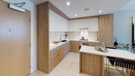 Located in the heart of South Park, Los Angeles, this modern residence at 1201 S Hope St offers a thoughtfully designed single-floor layout with a clean, contemporary aesthetic throughout. The open-plan living and dining area is anchored by a dramatic statement chandelier and a large gold-framed mirror, creating an elegant atmosphere with soft, neutral tones and refined finishes. Floor-to-ceiling windows flood the space with natural light and frame sweeping views of the downtown Los Angeles skyline, extending seamlessly to a private balcony. The kitchen features a sophisticated combination of warm wood cabinetry paired with high-gloss white upper cabinets, crisp white countertops, a stainless steel sink, and recessed lighting — offering both style and functionality. The bedroom continues the modern design language, showcasing hardwood flooring, a ceiling fan, and expansive glazed doors that open to the balcony, maintaining that ever-present connection to the city skyline. The bathroom is finished in light porcelain tile with a floating wood vanity, undermount sink, and a large mirror cabinet, creating a bright, spa-like retreat. Throughout the residence, a cohesive palette of whites, warm woods, and cool grays delivers a polished urban living experience in one of Los Angeles' most vibrant neighborhoods.