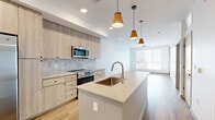 Located at 100 South 48th Street in Phoenix, AZ, this modern one-bedroom, one-bathroom unit offers a thoughtfully designed open-concept layout with contemporary finishes throughout. Light wood-look flooring flows seamlessly across the entire space, complementing the clean white walls and creating a bright, cohesive aesthetic.

The kitchen is a standout feature, anchored by a large center island with a single-basin sink and sleek light quartz countertops. Light wood cabinetry lines the walls, paired with a stone tile backsplash and a full suite of stainless steel appliances, including a side-by-side refrigerator, electric range, and built-in microwave. Stylish pendant lights hang above the island, adding warmth to the space.

The open living area is bathed in natural light from a large picture window with horizontal blinds, offering views of the surrounding Phoenix cityscape. A ceiling fan provides additional comfort. The bedroom is well-proportioned, featuring its own window with outdoor views, a ceiling fan, and access to a dedicated closet.

The bathroom presents a clean, modern design with wood-tone cabinetry, a glass-enclosed shower with matte black hardware, and consistent wood-look flooring. A private balcony rounds out the unit, providing an outdoor retreat. The space also includes an in-unit washer and dryer closet.
