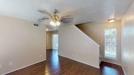 This two-story residence offers 2 bedrooms and 2.5 bathrooms across a well-organized floor plan. The main level features dark hardwood-style flooring throughout, a living area with a ceiling fan and staircase leading to the upper floor, and a nearby sliding glass door that brings in natural light. The kitchen is equipped with white cabinetry, dark granite-style countertops, a black electric range with an overhead exhaust fan, and ample storage space. A half bathroom on the main level provides added convenience for guests, featuring a granite-topped vanity and hardwood-style flooring.

Upstairs, both bedrooms are carpeted and include ceiling fans with light fixtures and windows that allow natural light in. One bedroom features a walk-in closet area and an en-suite bathroom with a dual-sink vanity topped with granite-style counters, a large mirror, and a separate toilet compartment. The second full bathroom also includes a granite-topped vanity. Textured ceilings are present throughout the home, and neutral warm-toned walls create a cohesive, move-in ready atmosphere across both floors.