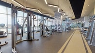 Located at 8340–8364 SW 84th St in Miami, FL, this professionally designed fitness center offers a comprehensive, single-floor workout facility built to accommodate a wide range of training needs. The space makes a strong first impression at entry, where a bold "MOTION" mural with a cityscape graphic and a rubber-floored running track with painted lane markings set an energetic, athletic tone.

The main workout floor is expansive and well-organized, featuring an extensive collection of strength-training machines, a full dumbbell rack, cable systems, and functional training equipment including TRX suspension trainers and medicine balls. A generous cardio zone lines the floor-to-ceiling glass window walls, housing treadmills and other aerobic machines that allow users to exercise while taking in outdoor views. Large wall-mounted displays and mirrored walls throughout further enhance the open, motivating environment.

A separate, glass-enclosed studio provides dedicated space for cycling classes, fitted with spin bikes, mirrored walls, and patterned glass partitions featuring a geometric yellow design. Geometric pendant lighting fixtures hang from high ceilings across the facility, complementing the modern navy, white, and gold color scheme. Oversized jersey-number graphics on structural columns reinforce the sports-inspired aesthetic throughout this dynamic and well-equipped fitness destination.
