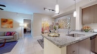 This well-appointed single-floor residence offers a thoughtfully designed open-concept layout that seamlessly connects the kitchen, dining, and living areas. The kitchen is a standout feature, showcasing granite countertops, rich dark wood cabinetry, stainless steel appliances including a range, microwave, and refrigerator, and a peninsula with an undermount sink that doubles as a breakfast bar. Elegant pendant lighting and a decorative mosaic mirror accent the space with contemporary flair. The adjoining dining and living areas flow naturally, with large-format tile flooring throughout. The living room benefits from a sliding glass door that invites natural light, complemented by a ceiling fan and vibrant wall art that adds a pop of color. Two bedrooms provide comfortable retreats, each with large windows, tile flooring, and plush area rugs. The primary bedroom features a serene, muted color palette with a soft accent wall, while the second bedroom offers ample natural light and warm, inviting tones. The bathroom is finished with granite countertops, a wood-toned vanity, large-format tile flooring, and a glass-enclosed walk-in shower, creating a clean and modern aesthetic throughout.