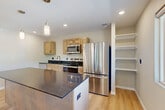 Located at 1800 Indian Hills Dr in Sioux City, Iowa, this 2-bedroom, 2-bathroom residence offers a thoughtfully designed single-floor layout. The open-concept kitchen and living area serves as the heart of the home, featuring light maple cabinetry, dark granite countertops, a central island with pendant lighting, and a full suite of stainless steel appliances including a French door refrigerator, electric range, and built-in microwave. An adjacent open shelving unit provides additional storage, while light oak hardwood-style flooring ties the space together. The living area is bright and welcoming, with recessed lighting and windows offering views of surrounding greenery. The spacious primary bedroom features plush carpet, a ceiling fan, and a dedicated walk-in closet with built-in shelving. The second bedroom is similarly comfortable, with carpet flooring, a ceiling fan, and a wide window framing outdoor tree views. Both bathrooms are finished with quality materials, including one featuring a stylish wood-grain vanity with a chevron pattern, white quartz countertop, and matte black fixtures. A utility room and closet round out the functional layout, making this a complete and well-equipped residence.