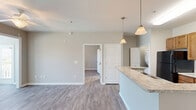 Located at 501 Hinson Dr in Myrtle Beach, SC, this one-bedroom, one-bathroom unit offers a well-planned single-floor layout with a neutral, modern aesthetic throughout. Light-toned luxury vinyl plank flooring runs seamlessly across all areas, complemented by crisp white baseboards and warm beige walls that create a clean, cohesive look.

The open-concept kitchen and dining area serves as the heart of the unit, featuring warm wood cabinetry, light granite-style countertops, and a peninsula island ideal for casual dining or food prep. Pendant lighting above the island adds a stylish touch, while black appliances — including a refrigerator, range, and microwave — provide a bold contrast. An in-unit washer and dryer area is conveniently located nearby.

The living and dining area receives generous natural light through multiple windows with blinds, including a door with a glass panel that opens to a private outdoor balcony with views of greenery.

The bedroom is a comfortable, well-proportioned retreat equipped with a ceiling fan with light fixture and a window overlooking the balcony, allowing for natural ventilation and outdoor views. A dedicated walk-in closet with multi-tiered wire shelving provides ample storage.

The full bathroom features a single-sink vanity with wood cabinetry, a large mirror with overhead lighting, and a tub-shower combination with grab bar support and clean white tile surround.