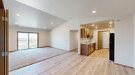 This single-floor residence offers a thoughtfully arranged layout across two bedrooms, a living room, kitchen, laundry, closet, and two hallways. The open-concept living and kitchen area is immediately welcoming, featuring vaulted ceilings that lend a sense of spaciousness beyond the unit's footprint. Light-toned hardwood-style flooring flows throughout the main living areas, transitioning to plush carpeting in the living room and bedrooms for added comfort.

The galley-style kitchen is well-appointed with warm wood cabinetry, light granite-style countertops, a stainless steel sink, and black appliances including a refrigerator and range. Recessed lighting illuminates the space efficiently. A sliding glass door in the living area opens to a private balcony, offering open views of the surrounding neighborhood and filling the room with natural light.

Both bedrooms are carpeted and feature wood-trimmed windows that frame outdoor views. The primary bedroom includes a dedicated closet and connects to the hallway layout for convenient access. The secondary bedroom is equally comfortable with generous natural light. A laundry area adds everyday practicality to this well-organized home. Neutral tones and clean finishes throughout create a bright, move-in-ready atmosphere.