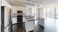 This thoughtfully designed high-rise unit occupies a single floor and offers an impressive blend of contemporary finishes and expansive urban views. The open-concept living and dining area features rich dark hardwood flooring and floor-to-ceiling windows that flood the space with natural light, with sliding glass doors leading to a private balcony overlooking the cityscape and surrounding greenery.

The gourmet kitchen is a standout feature, showcasing white shaker cabinetry, dark granite countertops, a mosaic tile backsplash, and a full suite of stainless steel appliances including a refrigerator, range, and microwave. A generous island with pendant lighting above provides additional prep and dining space, while track lighting illuminates the entire area.

The carpeted bedrooms offer a quiet retreat, each benefiting from large floor-to-ceiling windows with commanding views of the city and tree-lined streets below. A spacious walk-in closet with built-in wire shelving provides ample storage. The bathrooms are finished with white cabinetry, granite countertops, tile flooring, and clean modern fixtures, with one bath featuring a soaking tub with a glass partition. An in-unit washer and dryer complete the practical amenities of this well-appointed space.