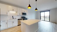 Located at 9201 W Mineral Point Rd in Madison, WI, this single-floor unit showcases a contemporary design with clean lines and a bright, neutral palette throughout. The open-concept kitchen serves as a central highlight, featuring white shaker cabinetry, a classic subway tile backsplash, light quartz countertops, and a full suite of stainless steel appliances including a gas range, built-in microwave, dishwasher, and French door refrigerator. A central island anchors the space, complemented by stylish black pendant lighting overhead. Light wood-tone flooring flows seamlessly through the main living and kitchen areas, enhancing the sense of openness and warmth.

The living area extends toward sliding glass doors that open to a private balcony, offering views of the surrounding neighborhood and allowing natural light to fill the space. Bedrooms are finished with plush neutral carpeting and large windows, with one room featuring a ceiling fan and an expansive window framing outdoor views. The bathroom presents a clean, modern aesthetic with warm wood-tone flooring, a soaking tub, and matte black fixtures throughout. The overall ambiance is modern, fresh, and move-in ready.