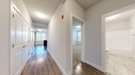This single-floor residence offers a well-organized layout that connects its living, kitchen, bedroom, and bathroom spaces through a central hallway finished with wood-style flooring. The hallway provides access to the various rooms and is accented by clean white trim and neutral wall tones throughout.

The kitchen is a standout feature, equipped with rich, dark-stained cabinetry offering generous storage, light stone-look countertops, and black appliances including a range and microwave. A peninsula with an integrated sink and pendant lighting above adds both functionality and visual interest, while a window allows natural light to fill the space.

The living area is spacious and open, featuring wood-style flooring and vertical blinds covering a large window or sliding door that draws in additional light. The bedrooms are carpeted for comfort, painted in soft neutral tones, and include panel-style doors with closet access.

The bathroom is cleanly appointed with a dark-cabinetry vanity, white countertop, a large mirror, tile flooring, and a full tub-shower combination. Throughout the unit, the consistent use of neutral tones, wood-style flooring, and white trim creates a cohesive, modern aesthetic.