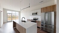 Located at 3597 Paramount Dr in West Lafayette, Indiana, this 2-bedroom, 2-bathroom unit offers a clean, modern aesthetic across a single floor. The open-concept kitchen and living area serves as the heart of the home, anchored by a generous kitchen island with a white quartz countertop, an undermount sink, and a sleek matte black faucet. Light wood cabinetry pairs with white upper cabinets and a classic subway tile backsplash, while stainless steel appliances — including a refrigerator, range, microwave, and dishwasher — complete the kitchen. A sculptural pendant light fixture adds a contemporary touch overhead. Large floor-to-ceiling windows flood the living space with natural light and frame outdoor views. Rich hardwood-style flooring runs throughout the main living areas and bedrooms, creating a warm, cohesive feel. The primary bedroom is generously sized, featuring a large window with outdoor views and ample closet space with double doors. Both bathrooms feature a modern design with concrete-look tile flooring, floating vanities, and matte black hardware and fixtures. The unit also includes a dedicated laundry space and multiple closets, ensuring excellent storage throughout.