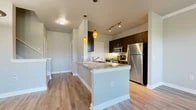 This thoughtfully designed one-bedroom, one-bathroom residence offers a comfortable and functional layout across a single floor. The entrance greets you with a staircase featuring a clean white handrail and built-in shelving tucked beneath the stairway, adding practical storage from the moment you arrive. The open-concept kitchen and living area form the heart of the home. The kitchen is well-appointed with dark espresso cabinetry, granite countertops, stainless steel appliances including a refrigerator, microwave, and range, and stylish pendant lighting over a peninsula that doubles as a breakfast bar. Warm wood-style flooring flows seamlessly throughout the living and dining areas, which benefit from generous natural light streaming through multiple windows and a glass-paned exterior door with outdoor views. The spacious bedroom features neutral tones, wood-style flooring, and access to a dedicated walk-in closet outfitted with wire shelving and organizational racks for ample storage. The full bathroom offers a tub-shower combination, a dark-cabinetry vanity with countertop space, and wood-style flooring. Neutral gray walls, white trim, and consistent finishes throughout give the space a cohesive, modern feel.