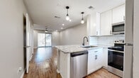 Located at 400 W Saint Elmo Rd in Austin, TX, this two-story, 2-bedroom, 3-bathroom home is thoughtfully laid out across two floors. The main level opens into a combined living, dining, and kitchen area finished with warm hardwood-style flooring and recessed lighting. A ceiling fan anchors the living space, which connects to the outdoors through a sliding glass door that invites natural light throughout. The kitchen is a standout feature, showcasing white shaker cabinetry with matte black hardware, a classic white subway tile backsplash, granite countertops with a peninsula that doubles as a breakfast bar, stainless steel appliances, and pendant lighting overhead. The bathrooms echo the kitchen's modern aesthetic with matching granite vanity tops, white cabinetry, and tub-shower combinations fully clad in large-format white subway tile with contrasting dark grout. Upstairs, the two bedrooms offer comfortable retreats with plush carpeting and ceiling fans. The primary bedroom includes a dedicated closet, providing practical storage. A utility room and laundry area add everyday convenience. The home's clean, neutral palette, consistent finishes, and efficient layout make it a well-appointed residence in South Austin.