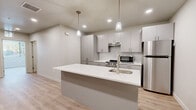 Located at 254 W 400 S in Salt Lake City, Utah, this single-floor unit offers a thoughtfully designed contemporary interior with a cohesive neutral color palette and light wood-style flooring throughout. The kitchen serves as the centerpiece of the space, showcasing flat-front gray cabinetry, a classic white subway tile backsplash, and a suite of stainless steel appliances including a gas range, microwave, and full-size refrigerator. A large kitchen island with a crisp white countertop and an integrated sink provides additional workspace and seating potential, while two elegant pendant lights hang above, adding a refined finishing touch. Recessed lighting complements the open feel of the kitchen and living areas. The bedroom is bright and welcoming, benefiting from a wide window with blinds that invite natural light and offer views of the surrounding greenery. The bathroom is finished with a gray single-vanity cabinet topped with a white countertop, a large mirror, wood-look flooring, and a walk-in shower enclosed by a sliding glass door. Clean lines and a consistent modern aesthetic unify every room, making this a well-appointed space in the heart of Salt Lake City.