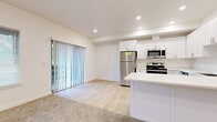 This thoughtfully designed single-floor residence offers a clean, contemporary aesthetic with a bright and open feel throughout. The heart of the home is the open-concept kitchen and living area, where light hardwood flooring transitions seamlessly into plush carpeting. The kitchen is equipped with stainless steel appliances—including a refrigerator, range, and microwave—complemented by crisp white shaker-style cabinetry, a white quartz countertop island, and a stainless steel dishwasher. Recessed lighting illuminates the space, while a sliding glass door fitted with vertical blinds invites natural light and provides access to the outdoors. The living area features a window with views of surrounding greenery, enhancing the sense of openness. The bedrooms are generously sized, each finished with soft wall-to-wall carpeting, neutral walls, and windows that bring in natural light. The bathroom is elegantly appointed with a patterned tile floor, white cabinetry with brushed nickel hardware, a quartz vanity countertop, an undermount sink, and a large mirror. Chrome fixtures and towel accessories complete the polished look. Overall, the space presents a fresh, move-in-ready environment with a neutral palette ideal for a variety of personal styles.
