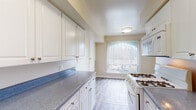 This single-floor residence offers a practical and comfortable layout designed to maximize functionality throughout. The living area is generously sized, featuring plush wall-to-wall carpeting, neutral warm-toned walls, and a ceiling fan overhead. Vertical blinds on a large sliding door allow natural light to fill the space while providing privacy. The kitchen is well-equipped with white cabinetry offering abundant storage, speckled blue-grey countertops, light wood-look flooring, a gas range, refrigerator, and a window that brings in additional natural light — creating a bright and efficient workspace. The bedrooms are carpeted and spacious, each featuring built-in closets with hanging rods. The primary bedroom includes access to a dedicated walk-in closet fitted with multi-level shelving, providing exceptional storage capacity. The bathrooms are cleanly finished with wood-look tile flooring, white vanities with matching countertops, and full tub-shower combinations. A hallway connects the living spaces to the private areas of the home, maintaining a logical and well-organized flow throughout. The overall aesthetic is clean, neutral, and move-in ready, offering a comfortable and functional living environment.