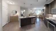This well-appointed single-floor residence offers a thoughtfully designed open-concept layout that seamlessly connects the kitchen, dining, and living areas. The kitchen serves as the heart of the home, featuring a large granite-topped island with an undermount sink, dark espresso cabinetry, stainless steel appliances including a refrigerator, range, and microwave, and pendant lighting that adds a modern touch. Wood-look flooring flows throughout the main living area, enhancing the sense of continuity and warmth.

The space includes two comfortable bedrooms, each finished with plush carpeting and neutral tones. One bedroom features a spacious walk-in closet, providing generous storage. Both rooms offer a calm, restful ambiance with ample room for furnishings.

The bathroom is clean and contemporary, showcasing a dark-cabinetry vanity with a white countertop, tiled flooring, and a full shower-tub combination. Natural light filters in through windows in the living area, brightening the open floor plan.

A dedicated in-unit laundry room with a full-size washer and dryer, complete with wire shelving for added storage, rounds out the practical amenities of this residence. The overall design balances modern aesthetics with functional living spaces.