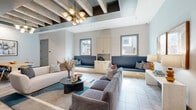 Located in Terrell, TX, this thoughtfully designed business center combines comfort and functionality across a single, well-appointed floor. The central living area sets an inviting tone, featuring a tray ceiling adorned with dark exposed wood beams and a striking brass multi-globe chandelier. Plush seating arrangements, including a velvet sofa and a cream sectional, are anchored by a bold teal-accented area rug atop polished tile flooring. Built-in navy upholstered bench seating lines the windowed wall, complemented by light wood cabinetry, creating a refined lounge atmosphere. Textured wallcoverings and soft blue-grey paint tones lend warmth and cohesion throughout. A dedicated dining or collaboration table with upholstered chairs provides an additional meeting area seamlessly integrated into the open layout. Three private offices offer focused work environments, each featuring light wood built-in desks, ergonomic seating, and distinctive arched windows with geometric patterned glass that introduce natural light while adding an artistic flair. Teal-patterned carpeting and curated artwork complete the offices, creating spaces that are both productive and visually engaging. This business center delivers a polished, contemporary environment ideal for professional use.