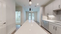 Located at 400 W. Main Street in Lewisville, TX, this thoughtfully designed 2-bedroom residence offers a clean, modern aesthetic across a single floor. The open-concept living area seamlessly combines the kitchen, dining, and living spaces into one bright, cohesive zone. The kitchen is a standout feature, showcasing a long waterfall-edge island with white quartz countertops, gray shaker-style cabinetry, a subway tile backsplash, stainless steel appliances including a dishwasher and refrigerator, and sleek pendant lighting. French doors at the far end of the living area invite abundant natural light and provide outdoor access, while a ceiling fan adds comfort to the space. Light wood-style flooring runs throughout the main living areas, contributing to a warm, contemporary feel. The primary bedroom offers comfortable proportions, plush carpeting, a dedicated closet, and a private en-suite bathroom. The second bedroom features a trio of windows that frame greenery outside, filling the room with natural light. Soft carpet and neutral walls carry through both bedrooms. An in-unit stacked washer and dryer is conveniently tucked within the layout. Recessed lighting and pendant fixtures throughout maintain a polished, modern ambiance.