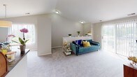 This single-floor residence offers a thoughtfully arranged layout with a bright, open feel throughout. The living room is a standout space, featuring soaring vaulted ceilings that amplify the sense of openness. Large windows on opposing walls flood the room with natural light, while plush carpeting and neutral wall tones create a warm, welcoming ambiance. A built-in ledge shelf adds architectural character and provides a functional display surface.

The kitchen is outfitted with white cabinetry, dark veined countertops, and wood-look flooring, offering a clean, functional workspace. An adjacent utility area houses in-unit washer and dryer appliances alongside additional storage space, adding considerable everyday convenience.

The primary bedroom benefits from a large window with outdoor views, vaulted ceilings, and soft carpeting. A walk-in closet provides ample storage. A second bedroom, similarly carpeted and well-proportioned, features vaulted ceiling details and direct access to a walk-in closet as well.

The full bathroom is finished with wood-look plank flooring, a white vanity with dark granite-style countertops, a large mirror, and a shower-tub combination. The neutral palette and clean finishes carry consistently throughout the home, contributing to a cohesive and comfortable living environment.