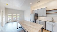 Located at 5235 SW Fairlawn Rd in Topeka, Kansas, this single-floor unit offers a clean, contemporary design throughout. The kitchen is a standout feature, showcasing gray shaker-style cabinetry, stone countertops, a white subway tile backsplash, and a full suite of stainless steel appliances including a refrigerator, range, microwave, and dishwasher. Open wood floating shelves add a warm contrast to the otherwise cool-toned palette. A large island with a stone top and sleek black metal base anchors the kitchen and provides generous workspace and gathering space.

The open living area flows naturally from the kitchen and is bathed in natural light through a set of French doors that open to a balcony with exterior views. Light wood-style flooring runs throughout the main living spaces, contributing to a bright, airy ambiance. The bedrooms feature plush carpeting, ceiling fans, and windows that bring in additional natural light.

The bathroom is finished with white cabinetry, stone countertops with an undermount sink, brushed gold fixtures, large-format tile flooring, and a tub-shower combination. An adjacent open shelving closet provides practical storage. Overall, the unit presents a modern, well-finished aesthetic with consistent attention to detail.