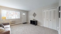 This single-floor residence offers a thoughtfully designed layout that balances comfort and functionality. The entryway welcomes visitors with soft carpeting, a classic white front door with a fanlight window, and a large closet with louvered bi-fold doors, providing generous storage from the moment you step inside. The living area flows naturally from the entry, featuring plush carpet, neutral walls, and a window that brings in natural light — creating a warm, relaxed atmosphere ideal for everyday living. Adjacent to the living space, a dedicated dining area accommodates a full dining set and features its own window, adding to the bright and airy feel of the space. The kitchen is equipped with warm wood cabinetry, dark granite-style countertops, tile-look flooring, and a full suite of black appliances including a gas range, dishwasher, and refrigerator. The primary bedroom is generously sized with carpeted floors, a large window with an exterior view, and ample room for a full furniture arrangement. A second bedroom offers similar comfort with its own window and natural light. The bathroom is clean and well-lit, featuring a white vanity with under-cabinet storage, a lighted mirror, tile-look flooring, and a bathtub. Baseboard heating is present throughout the unit.