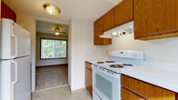 This three-floor residence is designed with practicality and functionality in mind. The kitchen is equipped with warm oak cabinetry, white electric range with overhead ventilation, and tile flooring. It opens directly into an adjacent living area, where a ceiling fan, carpeted floors, and a large window frame views of surrounding trees, allowing natural light to fill the space.

The main living areas feature neutral-toned carpet throughout, with wood-trimmed windows fitted with blinds providing both light control and privacy. Ceiling fans are present in key rooms, contributing to comfortable airflow. A dedicated utility nook includes tile flooring, a wall-mounted shelf, and a window overlooking the exterior.

Multiple carpeted rooms across the upper floors share a consistent design language: neutral walls, wood baseboards, floor vents, and windows with outdoor views of trees and the neighborhood. A staircase connects the levels, reinforcing the multi-story layout.

The basement level is unfinished, featuring a concrete floor, exposed joists overhead, drywalled perimeter walls, and small hopper windows. This open space offers significant potential for storage, a workshop, or future finishing into additional living areas.