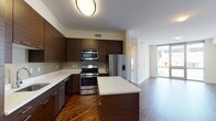 Located at Harbor Point in Stamford, CT, this one-bedroom, one-bathroom residence offers a thoughtfully designed single-floor layout with contemporary finishes throughout. The kitchen serves as a standout feature, showcasing rich dark wood cabinetry with sleek hardware, crisp white countertops, and a central island that provides additional prep and dining space. Stainless steel appliances — including a gas range, built-in microwave, and French-door refrigerator — complete the modern culinary setup. The kitchen flows seamlessly into the living area, which is bathed in natural light courtesy of floor-to-ceiling windows that frame views of the surrounding Harbor Point neighborhood. Rich hardwood flooring extends throughout the main living spaces, adding warmth and continuity to the open layout. The bedroom features plush carpeting and clean white walls, offering a quiet, neutral retreat. The full bathroom is finished with wood-look tile flooring, a dark wood vanity with a white countertop, and a tub/shower combination with white tile surround. Clean lines, neutral tones, and quality finishes define the overall aesthetic of this well-appointed residence.