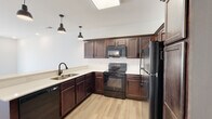 This single-floor unit on W Spring Dr in Ozark, Missouri offers a thoughtfully designed open-concept layout with modern finishes. Light wood laminate flooring runs throughout the space, creating a cohesive and bright aesthetic.

The kitchen is a standout feature, equipped with rich dark-stained cabinetry offering generous storage, light quartz countertops, and a full suite of black appliances including a refrigerator, electric range, over-the-range microwave, and dishwasher. A peninsula with an undermount sink and matte black faucet extends into the living area, providing additional prep space and a natural division between the kitchen and the open living room. Industrial-style pendant lighting accents the kitchen area, adding a contemporary touch. A skylight above the kitchen brings in additional natural light.

The living area is spacious and bright, featuring recessed lighting, a ceiling fan, and a sliding glass door that opens to an exterior view. A separate bedroom offers a ceiling fan, natural light through a window, and a clean, neutral palette. The bathroom includes a dark wood vanity with light countertop, an undermount sink, a round mirror, and stylish wall-mounted lighting fixtures.

The overall ambiance is clean, modern, and move-in ready.