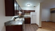 Located at 2350 Chalet Gardens Rd in Fitchburg, Wisconsin, this single-floor unit offers a practical and comfortable layout with consistent hardwood flooring throughout the main living areas. The kitchen is well-appointed with rich, dark wood cabinetry extending to the upper walls for generous storage, granite-toned countertops, a white electric range, and a full-size refrigerator. A built-in range hood and sink with lower cabinetry complete the functional kitchen setup, which opens toward the living area. The living room is open and airy, featuring light hardwood floors, baseboard heating, a wall-mounted air conditioning unit, and a window that brings in natural light with views of the surrounding greenery. An adjacent area provides additional open floor space, with warm-toned interior doors leading to the bedroom and other areas of the unit. The bedroom is a comfortable, well-proportioned room with the same hardwood flooring, a ceiling fan, and a sliding-door closet with built-in shelving and a hanging rod for ample storage. The bathroom includes a full-size soaking tub with a tiled shower surround in clean white, paired with a wall-mounted sink. The overall ambiance is clean, neutral, and move-in ready, suited for everyday living.