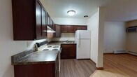 Located at 2350 Chalet Gardens Rd in Fitchburg, Wisconsin, this single-floor unit offers a practical and comfortable layout with consistent hardwood flooring throughout the main living areas. The kitchen is well-appointed with rich, dark wood cabinetry extending to the upper walls for generous storage, granite-toned countertops, a white electric range, and a full-size refrigerator. A built-in range hood and sink with lower cabinetry complete the functional kitchen setup, which opens toward the living area. The living room is open and airy, featuring light hardwood floors, baseboard heating, a wall-mounted air conditioning unit, and a window that brings in natural light with views of the surrounding greenery. An adjacent area provides additional open floor space, with warm-toned interior doors leading to the bedroom and other areas of the unit. The bedroom is a comfortable, well-proportioned room with the same hardwood flooring, a ceiling fan, and a sliding-door closet with built-in shelving and a hanging rod for ample storage. The bathroom includes a full-size soaking tub with a tiled shower surround in clean white, paired with a wall-mounted sink. The overall ambiance is clean, neutral, and move-in ready, suited for everyday living.