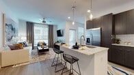 This single-story residence showcases a thoughtfully designed open-concept layout that seamlessly connects the kitchen, dining, and living areas. Light-toned hardwood-style flooring runs throughout, creating a cohesive and airy atmosphere. The kitchen is a standout feature, equipped with dark espresso cabinetry, stainless steel appliances, a subway tile backsplash, and a central island topped with light granite countertops. Pendant lighting above the island adds a refined touch, while bar-style seating makes it ideal for casual dining. The living area is bathed in natural light from multiple windows dressed with blinds and floor-to-ceiling curtains, complemented by a ceiling fan overhead.

The two bedrooms are well-appointed with large windows, dark curtain panels, and ample natural light. The primary bedroom features a dramatic upholstered headboard, while the second bedroom offers a bright, comfortable retreat. The bathroom mirrors the home's modern aesthetic with dark vanity cabinetry, a stone-topped counter, a large mirror, and a tiled tub-shower combination. A dedicated laundry area with a stacked washer and dryer unit and built-in shelving adds further convenience to this well-finished residence.