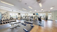 Located at 1200 Somerby Dr in Mobile, Alabama, this well-appointed fitness center spans a generous single-floor layout divided into two exercise rooms, offering a comprehensive environment for a wide range of workout routines. The facility is bright and open, with large windows lining the walls that flood the space with natural light and provide views of the surrounding greenery outdoors. Ceiling fans are positioned throughout to maintain comfortable airflow during workouts.

The main exercise room is expansively proportioned and features a robust selection of cardio equipment, including multiple treadmills, elliptical trainers, stair climbers, and stationary bikes. Flat-screen televisions are mounted at convenient viewing angles to keep users engaged during cardio sessions. A full-length wall mirror visually expands the space while supporting form checks during exercise. Rubber floor mats are laid across dedicated workout zones, complementing the warm terra-cotta tile flooring throughout.

The second exercise room provides a strength-training focus, housing a variety of resistance machines, a dumbbell rack with a graduated free-weight selection, weight benches, and a multi-use cable machine. Crown molding and recessed lighting add a refined architectural touch, giving the facility a polished, upscale ambiance. Together, both rooms provide a well-rounded, thoroughly equipped fitness experience.