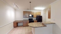 This single-floor residence offers a thoughtfully designed layout that balances functionality with comfort. The kitchen serves as a central highlight, featuring warm-toned wood cabinetry, granite-look countertops, and black appliances including a range, built-in microwave, and refrigerator. A curved breakfast bar provides a natural transition between the kitchen and the adjacent dining or workspace area, which includes a built-in desk with matching cabinetry—ideal for a home office setup. Track lighting and a pendant light illuminate the kitchen space effectively. Crown molding adds a refined architectural detail throughout the common areas.

The living area is finished with rich hardwood flooring and features a ceiling fan, providing an open and airy feel. Natural light filters in through sliding glass doors that lead to an outdoor area. The bedroom is carpeted for added comfort and includes a window overlooking greenery, as well as a ceiling light fixture. A closet with louvered doors offers convenient storage.

The bathroom is clean and functional, with tile flooring, a tub-shower combination with tiled surround, a toilet, and a vanity topped with granite-look counters and a wall mirror. Light tile flooring carries through the kitchen and bathroom, creating a cohesive aesthetic across the space.