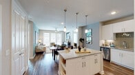 This single-floor residence offers a cohesive, modern aesthetic with an open-concept layout that seamlessly connects the kitchen, dining, and living areas. The kitchen is a standout feature, equipped with crisp white cabinetry, stainless steel appliances, a tiled backsplash, and a granite-topped island with bar seating illuminated by elegant pendant lighting. Rich hardwood-style flooring flows throughout the main living areas, grounding the space with warmth and continuity.

The living room is bright and inviting, benefiting from natural light that pours in through large French doors. A ceiling fan overhead and soft teal accent walls add personality and comfort to the space. The dining area connects naturally between the kitchen and living room, creating an ideal flow for everyday living and entertaining.

Both bedrooms continue the teal accent wall motif, each featuring ceiling fans, hardwood-style flooring, and windows that bring in natural light. The primary bedroom is accompanied by an en-suite bathroom complete with a granite vanity, glass-enclosed shower, and a walk-in closet with built-in shelving. A second full bathroom features a granite vanity and a shower-tub combination. The overall design balances modern finishes with a warm, livable atmosphere throughout.