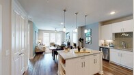 This single-floor residence offers a cohesive, modern aesthetic with an open-concept layout that seamlessly connects the kitchen, dining, and living areas. The kitchen is a standout feature, equipped with crisp white cabinetry, stainless steel appliances, a tiled backsplash, and a granite-topped island with bar seating illuminated by elegant pendant lighting. Rich hardwood-style flooring flows throughout the main living areas, grounding the space with warmth and continuity.

The living room is bright and inviting, benefiting from natural light that pours in through large French doors. A ceiling fan overhead and soft teal accent walls add personality and comfort to the space. The dining area connects naturally between the kitchen and living room, creating an ideal flow for everyday living and entertaining.

Both bedrooms continue the teal accent wall motif, each featuring ceiling fans, hardwood-style flooring, and windows that bring in natural light. The primary bedroom is accompanied by an en-suite bathroom complete with a granite vanity, glass-enclosed shower, and a walk-in closet with built-in shelving. A second full bathroom features a granite vanity and a shower-tub combination. The overall design balances modern finishes with a warm, livable atmosphere throughout.