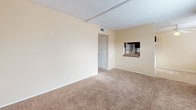 Located on Lomaland Drive in El Paso, Texas, this single-story home offers a straightforward, functional layout across several well-defined spaces. The living area is generously sized, featuring warm beige walls, plush carpeted flooring, and a textured ceiling. A pass-through window connects the living space to the kitchen, adding an open, communicative feel between the two areas. Natural light filters in through blinded windows, keeping the space bright and welcoming.

The galley-style kitchen is efficiently designed with dark espresso cabinetry lining both walls, providing ample storage space. Countertops run the length of the kitchen, accompanied by a double stainless steel sink, a gas range with oven, and a stainless steel refrigerator. Tile backsplash accents the cooking area, and tile flooring adds durability underfoot.

The bedrooms continue the warm, neutral palette with carpet flooring and windows that allow natural light to fill each room. The textured ceilings are consistent throughout the home, adding subtle visual interest.

The bathroom features a full tub and shower combination with floor-to-ceiling tile surround in a neutral gray tone. A dark-stained vanity with a light countertop and integrated sink completes the space, with tile flooring tying the room together cohesively.