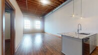 Located at 330 E Ninth St in Saint Paul, MN, this industrial-style loft masterfully blends historic character with contemporary finishes. The open-concept kitchen and living area serves as the heart of the space, showcasing soaring exposed wood beam ceilings with visible ductwork that reinforce the building's industrial heritage. Rich hardwood flooring runs throughout, complementing the original brick walls that line the perimeter and flood the space with warmth and texture. Large multi-pane windows invite generous natural light, enhancing the airy, loft-like atmosphere.

The kitchen is a standout feature, centered around a granite-topped island with an integrated sink, pendant lighting, white upper cabinetry, and a full suite of stainless steel appliances including a refrigerator, range, and microwave. A ceiling fan provides additional comfort in the expansive living area.

The bathroom is thoughtfully finished with a gray vanity, mosaic tile accents, subway tile wainscoting, and a patterned marble-style floor. A dedicated laundry area with a walk-in closet adds everyday convenience. Warm wood interior doors and trim throughout tie the modern updates seamlessly to the building's original industrial character.