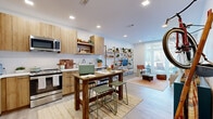 Located at 100 Whitwell St in Quincy, MA, this thoughtfully designed one-bedroom, two-bathroom residence offers an efficient and stylish single-floor layout. The open-plan kitchen and living area serves as the heart of the home, where light wood cabinetry, white subway tile backsplash, and stainless steel appliances — including a full-size refrigerator, range, and microwave — create a functional and modern kitchen. A dining area flows naturally from the kitchen, making the space ideal for both cooking and entertaining. The living room is bright and inviting, featuring large sliding glass doors that flood the space with natural light and provide access to an outdoor area. Recessed lighting and light wood-tone flooring carry throughout, lending a cohesive, contemporary feel. The bedroom is a comfortable retreat with plush carpet flooring, a large window with outdoor views, and ample room for furnishings. A dedicated closet provides organized storage with full-length hanging rails and shelving. The two bathrooms are finished with neutral tile, clean white walls, and wood-accented vanities. One bathroom features a glass-enclosed walk-in shower with subway tile surround, adding a polished touch. Overall, the residence balances modern finishes with a warm, livable ambiance.