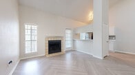 Located at 6000 Oakmont Trail in Fort Worth, TX, this two-bedroom, two-bathroom residence spans two floors, offering a well-designed layout with distinct living and sleeping areas. The main floor impresses with soaring vaulted ceilings and stylish herringbone-patterned wood-look flooring that flows throughout the living area. A tile-surround wood-burning fireplace serves as a focal point, flanked by multiple windows that invite abundant natural light. A pass-through opening connects the living space to the kitchen, which features white cabinetry, light stone countertops, a subway tile backsplash, and stainless steel appliances. A staircase with white metal railings leads to the upper floor. Both bedrooms are carpeted and include ceiling fans, ample windows, and closet access. The bathrooms are finished with herringbone-pattern flooring, white cabinetry, stone countertops, and large framed mirrors — one bath includes gold-framed mirrored sliding closet doors. An in-unit laundry area with washer and dryer adds everyday convenience. The space combines a clean, neutral palette with thoughtful finishes throughout.