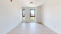 Located in East Harlem at 205 E 110th Street, this thoughtfully designed two-bedroom, two-bathroom residence offers a clean, modern aesthetic across a well-organized single-floor layout. Light-toned hardwood floors run throughout, complementing the crisp white walls and creating a bright, cohesive atmosphere.

The living area connects seamlessly to a kitchen outfitted with wood-accented cabinetry, a stainless steel range, and a sleek black fixture sink. Both bedrooms are generously proportioned, with the primary bedroom featuring corner placement and floor-to-ceiling black-framed windows that flood the room with natural light and frame striking panoramic views of the Manhattan skyline. The secondary bedroom also benefits from black-framed windows with open city views, and includes a built-in double closet for ample storage.

The two bathrooms are finished with elegant marble-style tile extending from floor to ceiling. One bathroom offers a soaking tub with a handheld shower and matte black fixtures, while the other showcases expansive windows with breathtaking skyline views, a vessel sink, and refined marble surroundings. The consistent use of high-contrast black hardware and natural materials throughout gives the residence a polished, contemporary character.