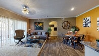 This single-story, 2-bedroom, 3-bathroom residence features a thoughtfully designed open-concept layout that seamlessly connects the living room, dining area, and kitchen. The living room is finished with plush carpet and includes a sliding glass door that opens to an outdoor patio, allowing natural light to fill the space. Adjacent to it, the dining area showcases rich hardwood-style flooring, crown molding, and warm accent walls. The kitchen is well-equipped with light wood cabinetry, dark granite-style countertops, black appliances including a refrigerator, range, microwave, and dishwasher, complemented by a mosaic tile backsplash and a convenient pass-through to the laundry area. The primary bedroom offers comfortable carpeting, a large window, and a ceiling fan, while the second bedroom also features carpet flooring and ample natural light from multiple windows. All three bathrooms include tub-shower combinations, with at least one featuring granite-style countertops and light wood vanity cabinetry with hardwood-style flooring. A dedicated laundry space, a hallway, and a closet round out the functional layout of this well-designed home.