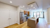 Located in Philadelphia's Northern Liberties neighborhood, this well-appointed 1-bedroom, 2-bathroom residence at 517 Poplar Street offers a thoughtfully designed single-floor layout with modern finishes throughout. The open-concept kitchen and living area serves as the heart of the home, featuring a large granite-topped island with an undermount sink and brass faucet, sleek stainless steel appliances including a gas range and French door refrigerator, and a striking combination of high-gloss white and warm wood cabinetry with a tile backsplash. Recessed lighting and a stylish tray ceiling detail add architectural interest overhead, while light-toned hardwood floors extend seamlessly throughout the entire residence. The living area is bright and airy, benefiting from floor-to-ceiling sliding glass doors that open to a private balcony with views of the surrounding neighborhood. The generously sized primary bedroom also enjoys direct outdoor access through large sliding glass doors, filling the room with natural light. Two well-appointed bathrooms include a standout walk-in shower clad in linear gray tile with penny-round mosaic flooring. A hallway connects the living spaces with practical flow, completing this refined and contemporary urban residence.