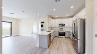 Located at 3724 SW 12th Pl in Fort Lauderdale, FL, this contemporary single-floor residence offers a clean, modern design throughout. The open-concept layout connects the kitchen and living area seamlessly, creating a bright and airy atmosphere enhanced by recessed lighting and light wood-tone flooring that extends throughout the space.

The kitchen is a standout feature, equipped with stainless steel appliances including a refrigerator, range, over-the-range microwave, and dishwasher. Shaker-style cabinetry in crisp white and light gray tones is paired with white quartz countertops and black hardware accents. A peninsula with an undermount sink provides additional prep space and casual seating potential. A stacked washer and dryer unit is conveniently integrated nearby.

The living area is generously proportioned and bathed in natural light, with large sliding glass doors opening to a private balcony that overlooks lush greenery. The bedrooms are well-sized, each featuring ceiling fans, large black-framed windows with outdoor views, and access to walk-in closet space.

The bathrooms are finished with elegant large-format marble-look tile on both the floors and tub surround, complemented by gray shaker-style vanities with white countertops and brushed nickel fixtures, delivering a polished, spa-like aesthetic throughout.