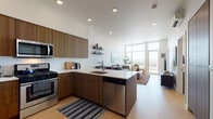 This thoughtfully designed one-bedroom residence combines modern aesthetics with functional living across a single floor. The open-concept kitchen flows seamlessly into the living area, anchored by flat-front walnut-toned cabinetry, white quartz countertops, a peninsula island with an undermount sink, and a full suite of stainless steel appliances including a gas range, microwave, and dishwasher. Light oak hardwood flooring runs throughout, lending warmth and continuity to the space. The living room is a bright, airy retreat defined by floor-to-ceiling windows and glass doors that frame expansive city and hillside views, flooding the space with natural light. The bedroom offers a generous sliding-door closet, light hardwood flooring, and a large picture window showcasing scenic outdoor views. Both bathrooms are finished with clean, neutral tilework and frameless glass-enclosed walk-in showers with handheld fixtures and backlit vertical lighting. A stacked in-unit Whirlpool washer and dryer adds everyday convenience. Recessed lighting throughout, crisp white walls, and a clean architectural palette create a cohesive, contemporary ambiance well-suited for modern urban living.