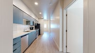 Located at 140 W Second Ave in Mesa, Arizona, this well-designed two-bedroom, two-bathroom residence offers a clean, contemporary aesthetic throughout its single-story layout. Light wood-style flooring runs continuously through the space, lending a cohesive and modern feel to every room.

The galley-style kitchen is a standout feature, showcasing slate-blue flat-front cabinetry extending floor to ceiling, crisp white countertops, and a full suite of stainless steel appliances including a refrigerator, electric range, microwave, and dishwasher. Recessed lighting illuminates the kitchen corridor, which opens toward the living area at the far end.

The primary bedroom is generously appointed with dual windows that invite natural light and a ceiling fan overhead for comfort. The second bedroom also benefits from large windows and tall ceilings, creating an airy atmosphere. A dedicated walk-in closet provides practical storage with full-length hanging rods and shelving.

Both bathrooms continue the blue-gray cabinetry theme, featuring vanities with white countertops, framed mirrors, and wall-mounted storage. One bathroom includes a standalone walk-in shower, while the other offers a vanity with overhead cabinet. The overall design is clean, minimalist, and move-in ready, making this Mesa residence an efficient and attractive living space.